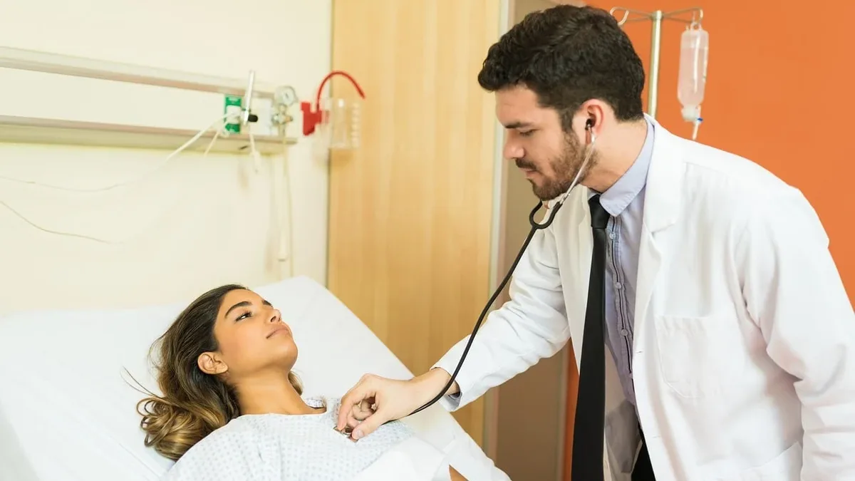 A doctor using a stethoscope to listen to a patient's heartbeat in a hospital room.