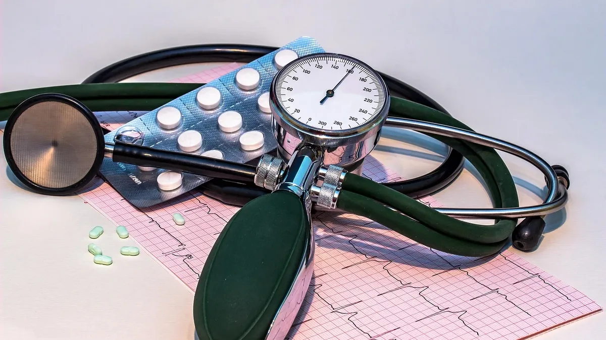 A stethoscope, a blood pressure cuff, a blood pressure gauge, a blister pack of pills, and a piece of graph paper with an electrocardiogram (ECG) tracing on it.